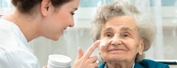 caretaker applying face cream to older woman