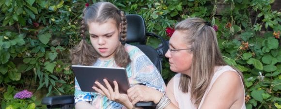 child with disability using tablet with special needs care assistant