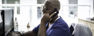 A woman with short blond hair and blue shirt on the phone at a 988 hotline working with a behavioral health patient