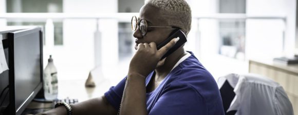 A woman with short blond hair and blue shirt on the phone at a 988 hotline working with a behavioral health patient