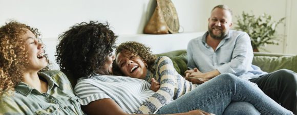 A co-parenting man and woman on the couch with their two daughters laughing