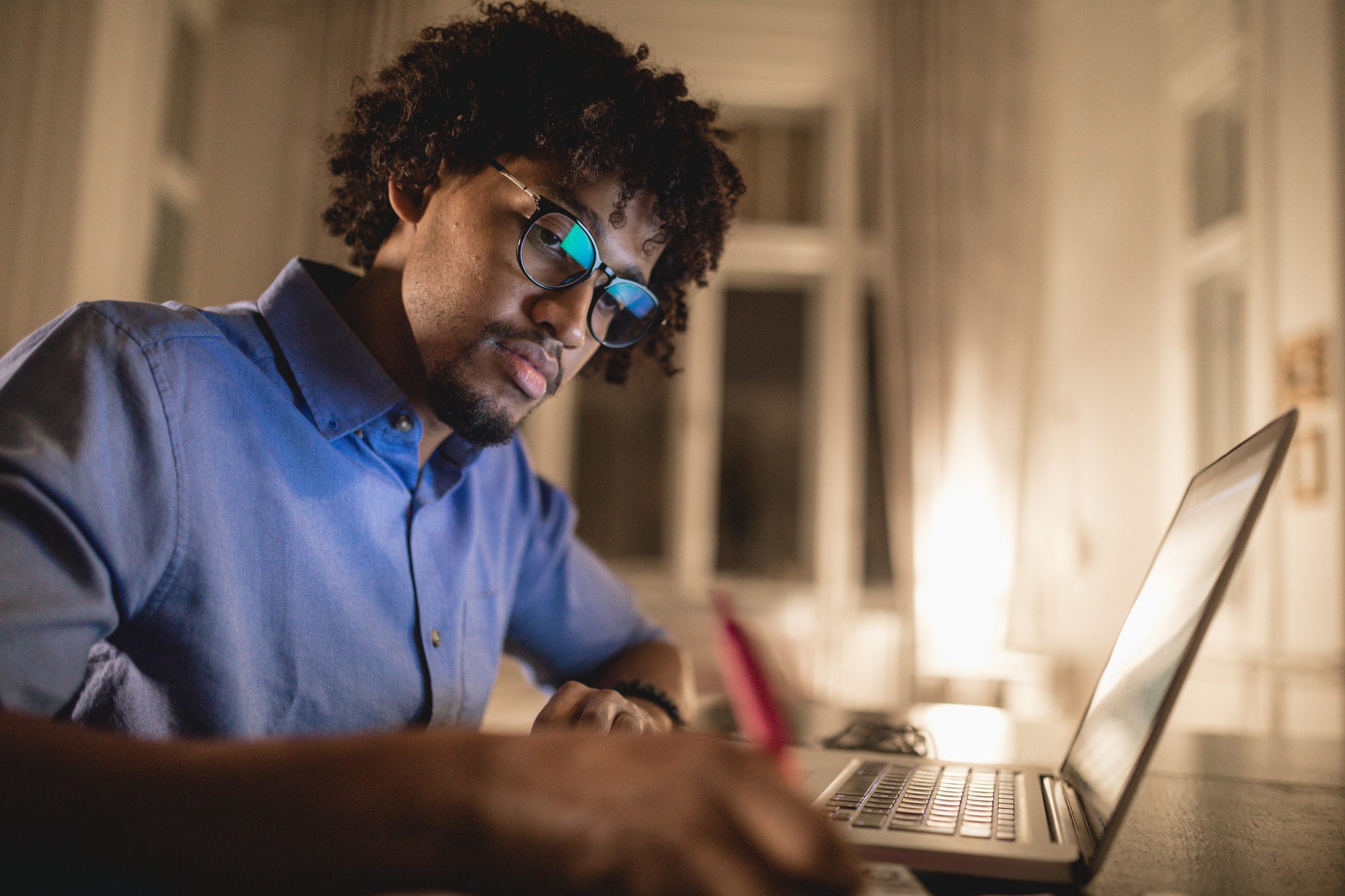 Young and determined black student studying at night at home, with a help of a laptop computer.