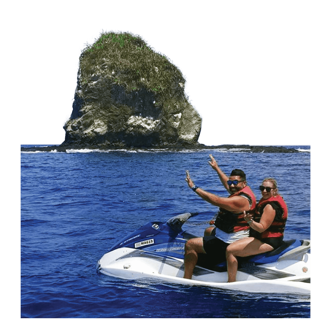 A man and a woman sit on a jet ski in the ocean near with an island in the background.