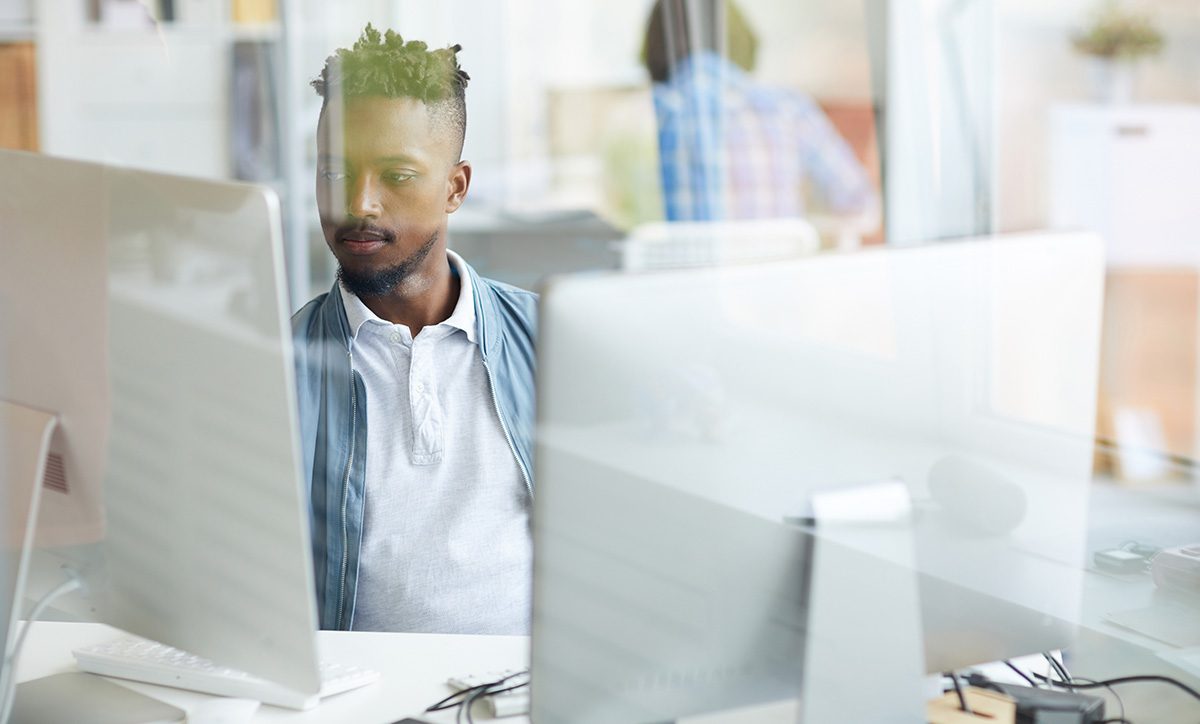 man works at a computer behind glass